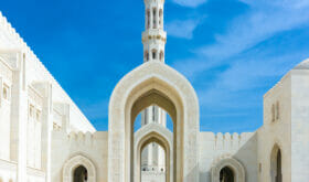 Woman in black Abaya Gown walking towards the giant arch in the famous Sultan Qaboos Grand Mosque in Muscat, Oman, Middle East, Arabia.